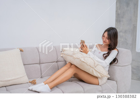 A Young Woman is Relaxing Comfortably on a Couch with her Smartphone and Cozy Pillow A Young Woman is Relaxing Comfortably on a Couch with her Smartphone and Cozy Pillow 130388382