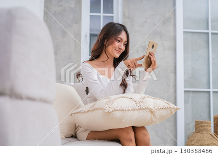 A Relaxed Young Woman Happily Using Her Smartphone in a Cozy Living Room Space A Relaxed Young Woman Happily Using Her Smartphone in a Cozy Living Room Space 130388486