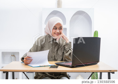 A Young Woman Actively Engaged in Online Learning with Her Laptop and Notes in Front 130388506