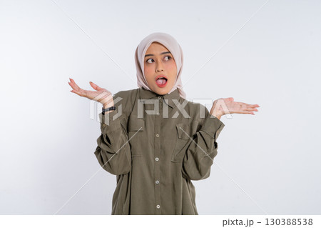 A Young Woman Wearing a Hijab is Expressing Her Surprise with Her Hands Raised Up 130388538