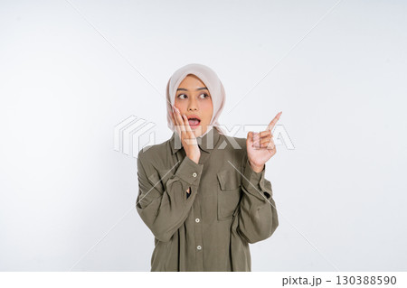 Surprised Woman in Hijab Pointing with Shocked Expression on White Background 130388590