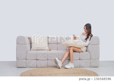 Woman Relaxing on a Modern Sofa with a Phone in a Minimalist Living Room 130388596