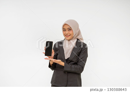 A confident businesswoman in a hijab presents a smartphone, showcasing modernity 130388643