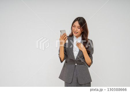 Young Businesswoman Excitedly Engages with Smartphone in Professional Attire 130388666
