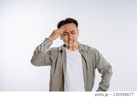 A Young Man in Casual Wear with a Stressful Expression and Headache on a Simple Background 130388677