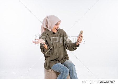 A joyful and excited woman wearing a hijab is engaging with her smartphone device A joyful and excited woman wearing a hijab is engaging with her smartphone device 130388707