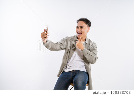 Cheerful Young Man Taking a Selfie with a Smartphone in a Studio Setting 130388708