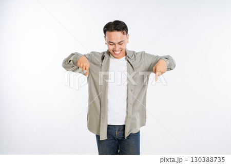 Cheerful Young Man Pointing Downwards with a Smile in a Bright Studio Setting 130388735