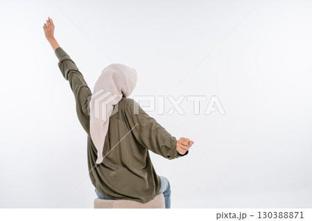 A Joyful Young Woman is Celebrating with Her Hands Raised while in a Casual Outfit 130388871