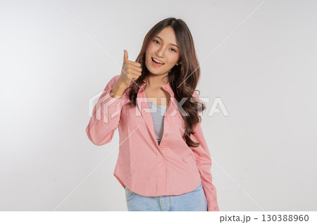 A cheerful young woman gives a thumbs up gesture while dressed in a stylish outfit, A cheerful young woman gives a thumbs up gesture while dressed in a stylish outfit, 130388960