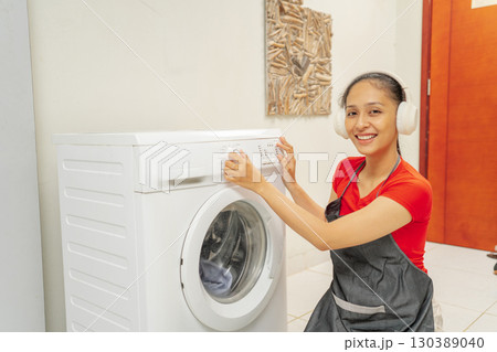 A Happy Young Woman is Using a Washing Machine in the Comfort of Her Home A Happy Young Woman is Using a Washing Machine in the Comfort of Her Home 130389040