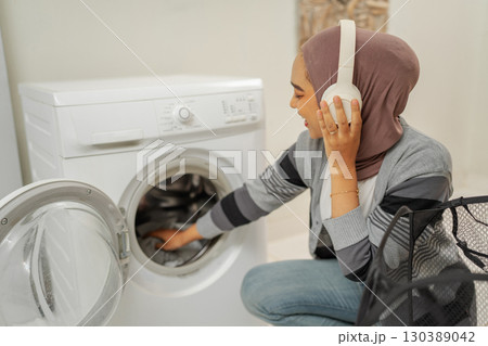 A woman in headphones operates a washing machine, enjoying music while doing chores 130389042
