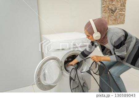 A woman wearing headphones is doing laundry in a contemporary home setting A woman wearing headphones is doing laundry in a contemporary home setting 130389043