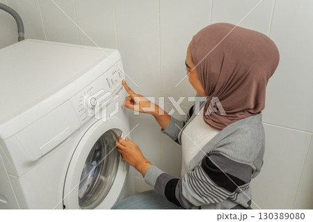 A woman is diligently using a modern washing machine in her bright laundry room A woman is diligently using a modern washing machine in her bright laundry room 130389080