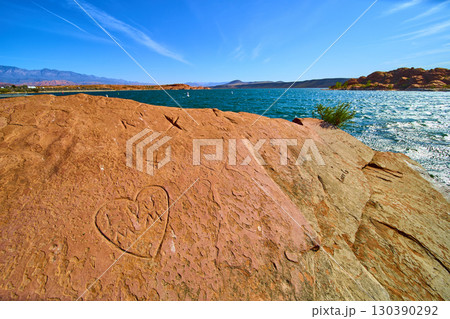 Red Rock Heart Carving by Desert Lake with Blue Water Low Eye Level Perspective 130390292