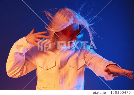 Creative portrait of a man with long white hair in a dynamic pose, wearing sunglasses, against a gradient blue and orange background, conveying energy and artistic expression Creative portrait of a man with long white hair in a dynamic pose, wearing sunglasses, against a gradient blue and orange background, conveying energy and artistic expression 130390479