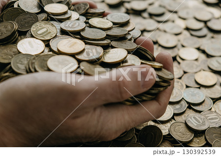 male hands holding various coins with numerous others scattered on table. closeup. male hands holding various coins with numerous others scattered on table. closeup. 130392539