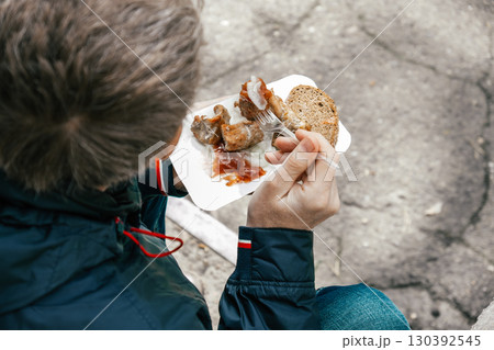 man enjoying street food barbecue, bread, sauce while sitting outdoors in casual setting. closeup. 130392545