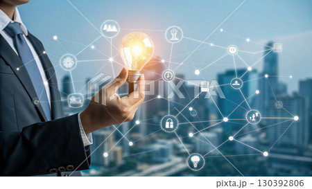 A businessman holds a glowing light bulb symbolizing innovation and new ideas, connected to a digital network representing technology and business solutions 130392806
