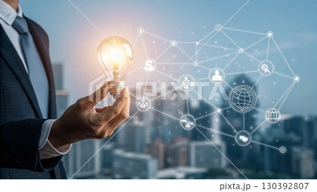 A businessman holds a glowing light bulb symbolizing innovation and new ideas, connected to a digital network representing technology and business solutions 130392807