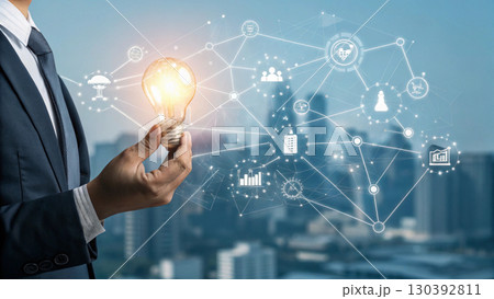 A businessman holds a glowing light bulb symbolizing innovation and new ideas, connected to a digital network representing technology and business solutions A businessman holds a glowing light bulb symbolizing innovation and new ideas, connected to a digital network representing technology and business solutions 130392811