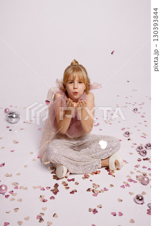 Smiling girl blowing confetti sitting on floor with Christmas balls studio shot 130393844