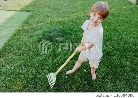 Playful boy working in the garden, enjoying outdoor activities with a bright smile, wearing casual clothes and standing on lush green grass in the sunlight. Playful boy working in the garden, enjoying outdoor activities with a bright smile, wearing casual clothes and standing on lush green grass in the sunlight. 130394006