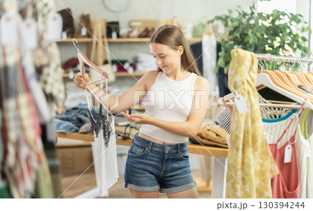 Positive teenage girl choosing something for summer in clothing store 130394244