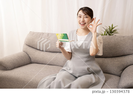 ソファーに座って預金通帳を持つ妊娠8ヶ月の女性 130394378