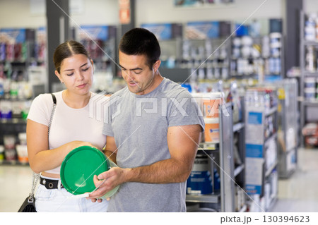 Husband buyer with paint container in hand consults with wife and examines can of enamel dye 130394623