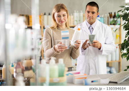 Young woman choosing cream while pharmacist offering in drugstore 130394684