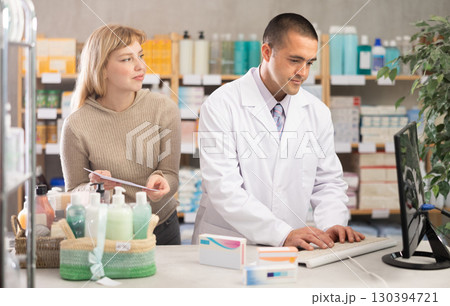Man pharmacist is working at computer, communicate with girl customer 130394721