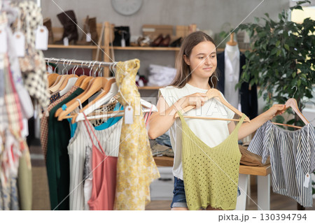 Positive teenage girl choosing something for summer in clothing store Positive teenage girl choosing something for summer in clothing store 130394794