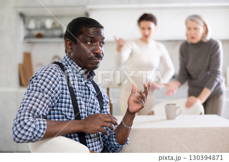 Middle-aged man sitting at the kitchen table with his back to women quarreling to him Middle-aged man sitting at the kitchen table with his back to women quarreling to him 130394871