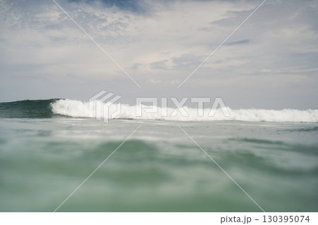 Ocean wave cresting under cloudy sky 130395074