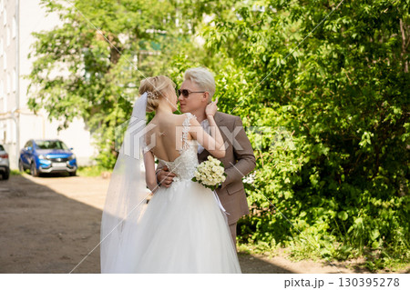 Couple joyfully embraces in wedding attire surrounded by greenery Couple joyfully embraces in wedding attire surrounded by greenery 130395278