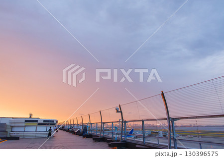 夕焼けの羽田空港のデッキ。 離発着する旅客機と夕暮れの東京の町並みが見える。2025 130396575