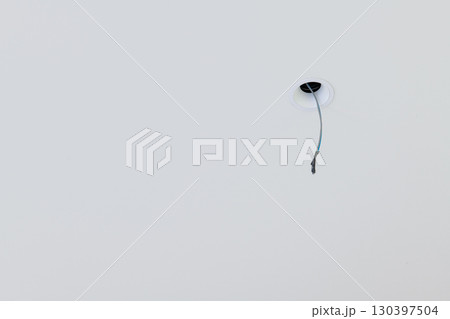 Close up detail of lone electrical wire hanging from white ceiling during house renovation. minimal construction scene shows an unfinished space with room for design Close up detail of lone electrical wire hanging from white ceiling during house renovation. minimal construction scene shows an unfinished space with room for design 130397504