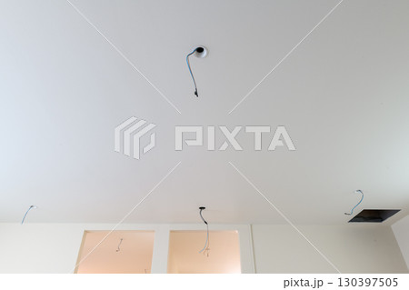 Detail view of electrical wiring hanging from ceiling during house renovation. construction project shows exposed wires for future lighting in clean white room 130397505