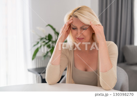 Blonde middle aged woman sitting alone at kitchen table, covering face with hands, crying with despair and sadness, emotional breakdown at home Blonde middle aged woman sitting alone at kitchen table, covering face with hands, crying with despair and sadness, emotional breakdown at home 130398270