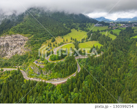 This aerial view showcases winding asphalt roads through the lush green hills of the Alps, with dramatic cloud cover enhancing the serene beauty of a road trip adventure. This aerial view showcases winding asphalt roads through the lush green hills of the Alps, with dramatic cloud cover enhancing the serene beauty of a road trip adventure. 130399254