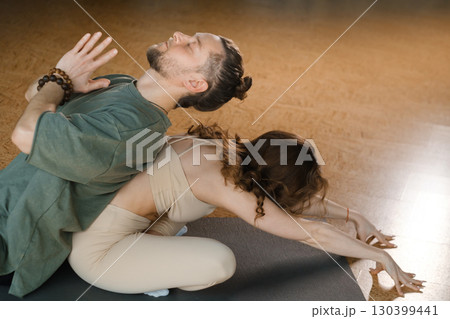 Couple practicing yoga together in a calm studio setting with warm lighting and natural decor during a serene afternoon session 130399441