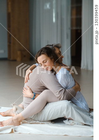 Couple engaging in a warm embrace during a morning meditation session in a bright, serene studio space 130399459
