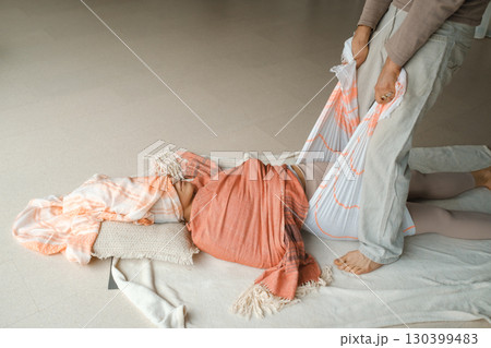 Wellness session in a serene studio focuses on relaxation techniques using a supportive wrap during a tranquil midday practice 130399483
