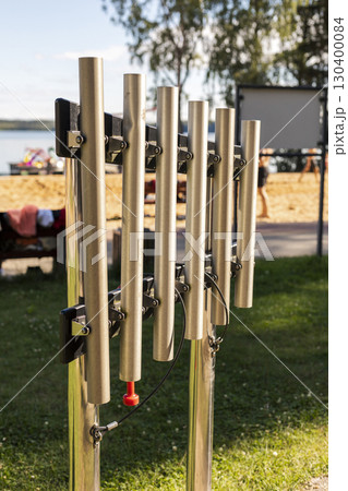 A set of metal tubes is mounted on a stand at a beachside location, creating an inviting atmosphere for music lovers as visitors relax in the background A set of metal tubes is mounted on a stand at a beachside location, creating an inviting atmosphere for music lovers as visitors relax in the background 130400084