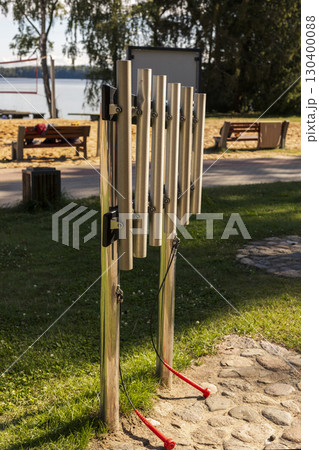 Visitors can enjoy making sounds on the metallic musical instruments located near the water's edge in a serene park setting. The instruments are designed for public use and creativity 130400088