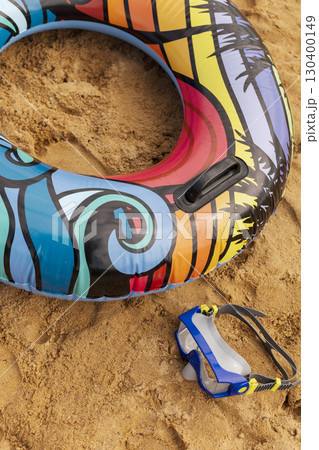 An inflatable tube with vibrant patterns rests on warm sand beside a pair of swimming goggles, inviting beachgoers to enjoy a sunny day filled with water activities and relaxation 130400149