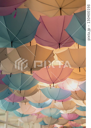 A vibrant display of umbrellas in shades of pink, blue, and cream adorns the ceiling of a lively indoor area, enhancing the cheerful atmosphere of the afternoon setting A vibrant display of umbrellas in shades of pink, blue, and cream adorns the ceiling of a lively indoor area, enhancing the cheerful atmosphere of the afternoon setting 130400198