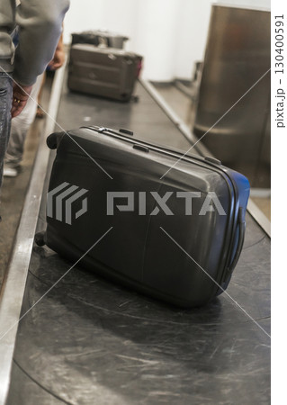 Travelers at the airport are collecting their luggage from the baggage claim area, showcasing various suitcases, as excitement fills the air 130400591