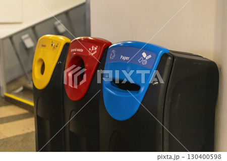 Colorful recycling bins labeled for paper, general waste, and plastic are positioned against a wall in a public space, promoting recycling and waste separation Colorful recycling bins labeled for paper, general waste, and plastic are positioned against a wall in a public space, promoting recycling and waste separation 130400598